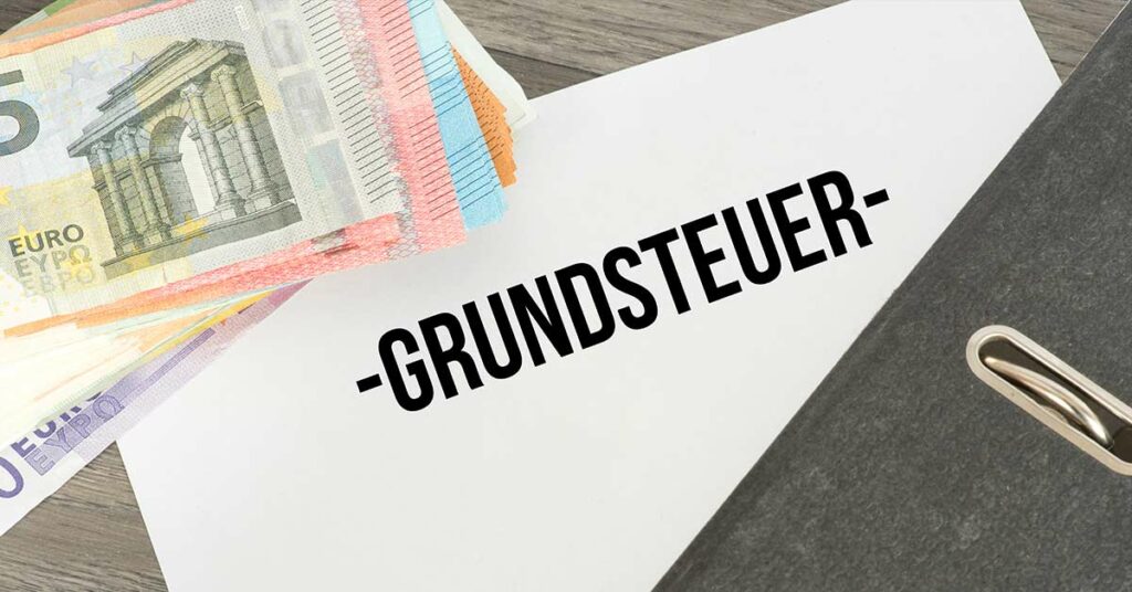 Auf einem Schreibtisch liegen Geldscheine, ein Ordner und ein Papier mit dem Wort "Grundsteuer" - Grundsteuer